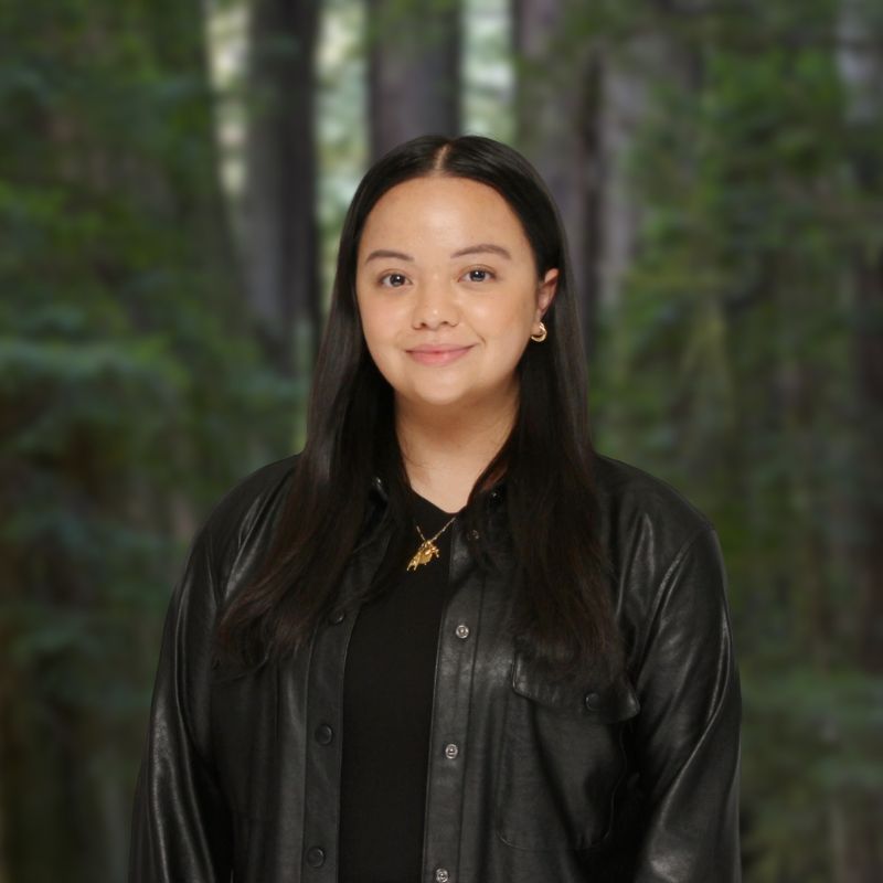 Headshot of Emily Woo wearing a black leather jacket with a forest background