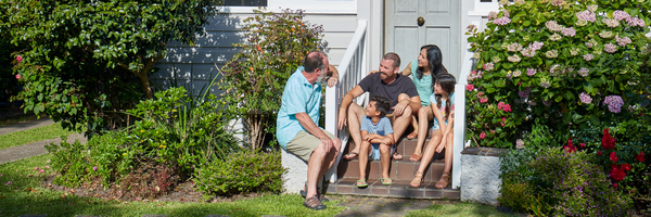 Image of an intergenerational family sitting on a doorstep of the house.